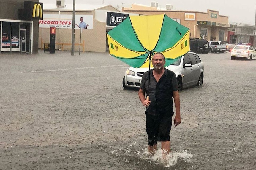 A man stands in a flooded street holding an inside-out umbrella.