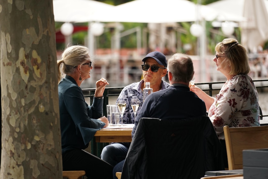 Four people eat lunch at an outdoor table on a sunny Melbourne day.