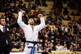 Leandro Lo stands in front of a crowd with his arms held up after he wins a jiu-jitsu tournament 