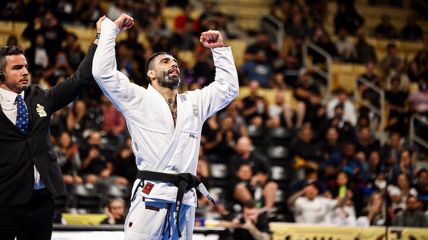 Leandro Lo stands in front of a crowd with his arms held up after he wins a jiu-jitsu tournament 