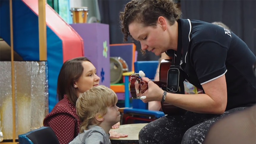 Lee Strickland plays guitar to a young child with blonde hair.