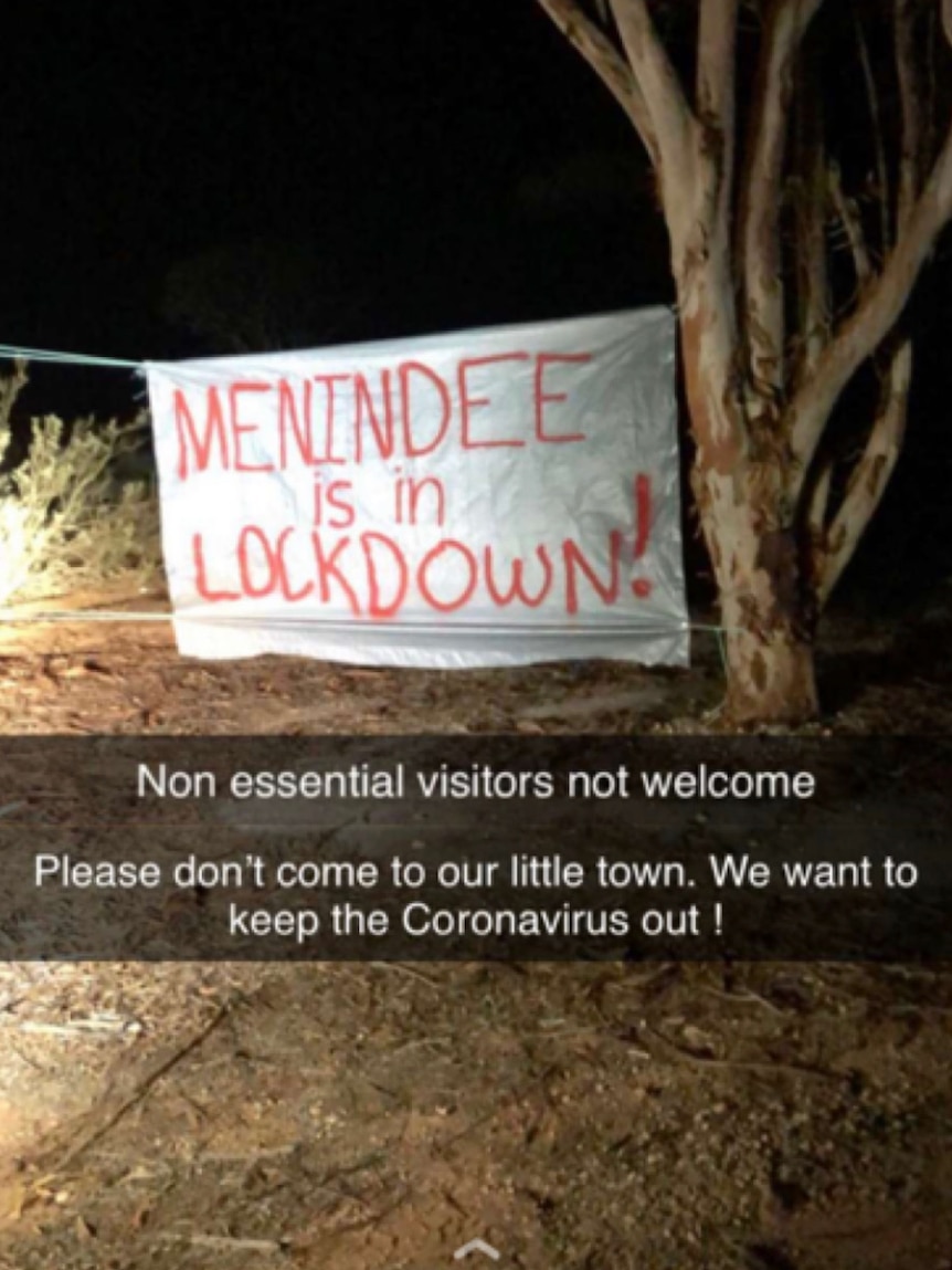 Red lettering on a white sheet suspended between trees reads 'Menindee is in lockdown'.
