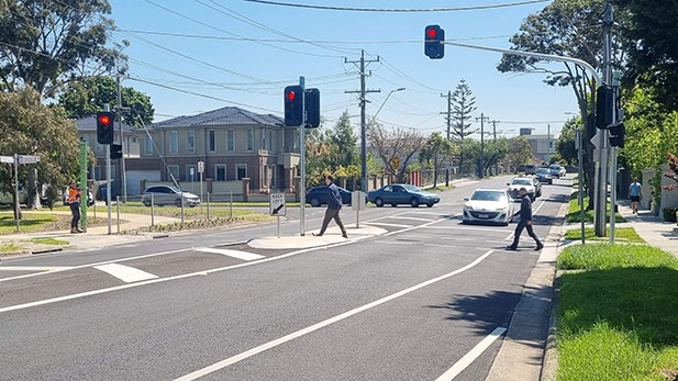 A man crosses a pedestrian crossing on a sunny day.