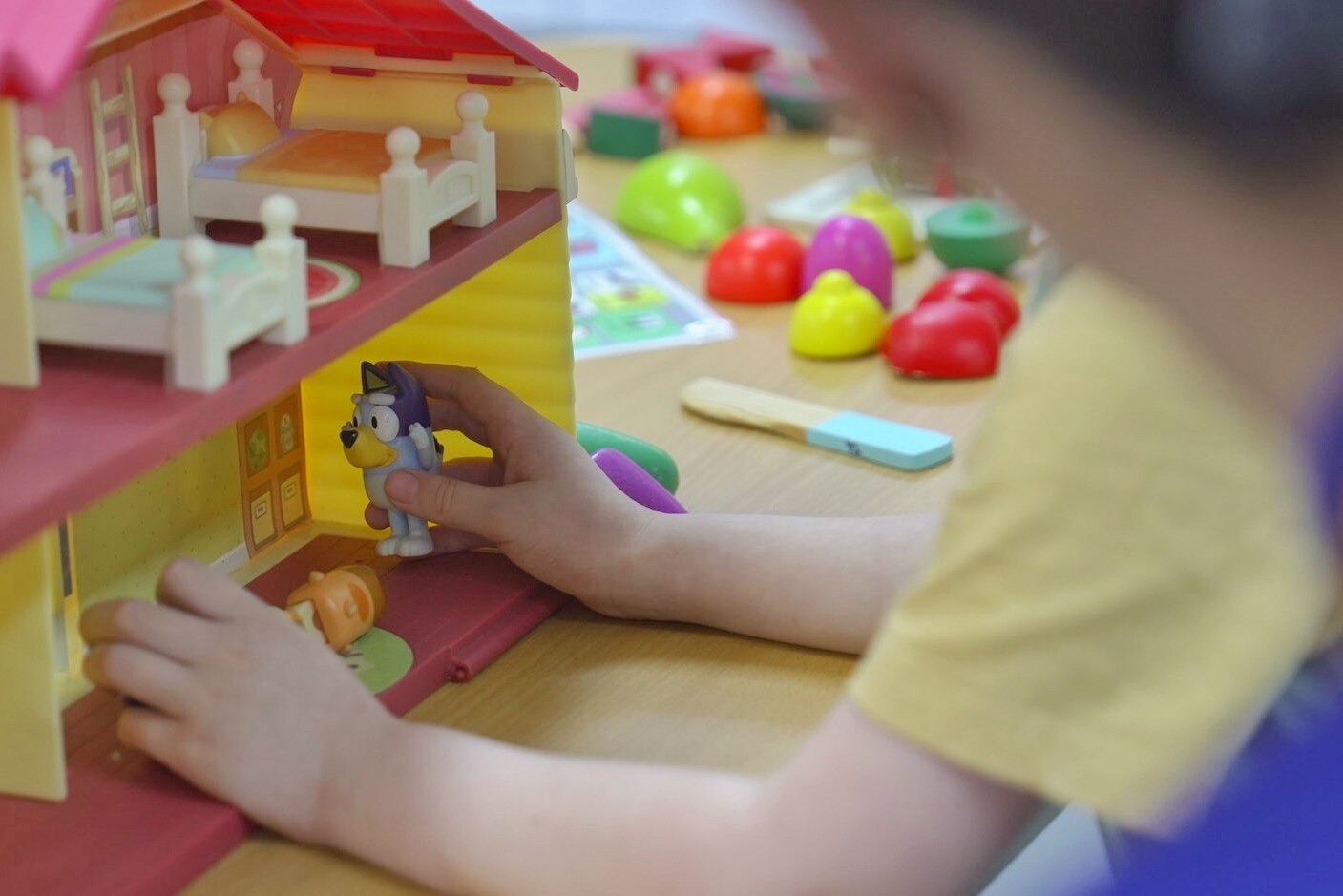 A non-identifiable child playing with a small Bluey toy and colourful dollhouse.