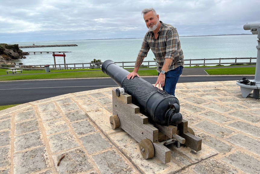 A man with a black cannon overlooking a bay with a sign with Chinese writing on it