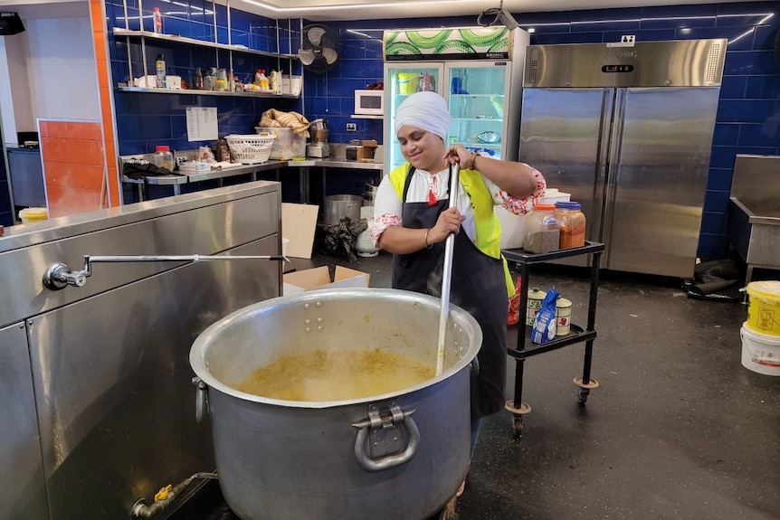 A Sikh lady stirs a huge pot of curry. 