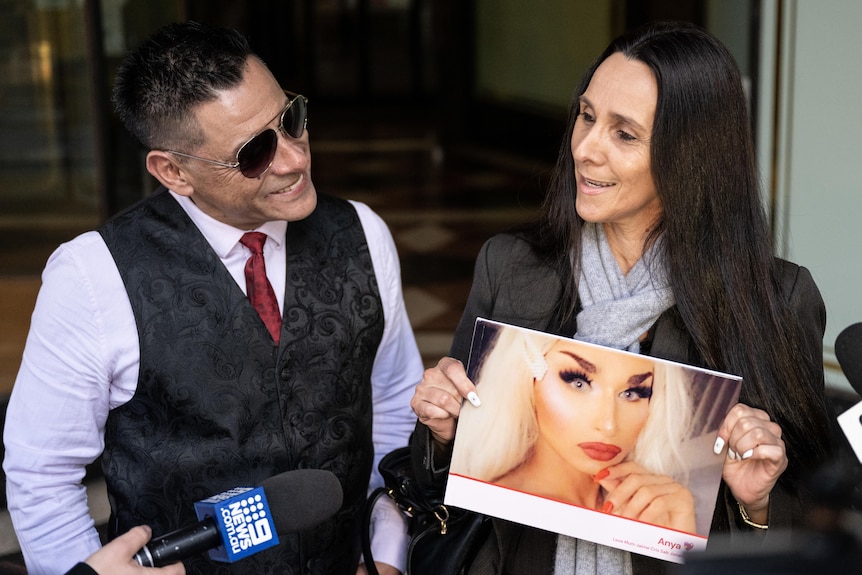 a man and woman stand outside court holding a picture of Anya Bradford