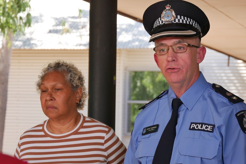 A police officer with a hat on stands beside a woman in a stripey t-shirt