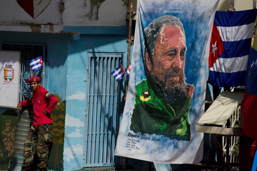 A militia member stands next to a painting of Fidel Castro.