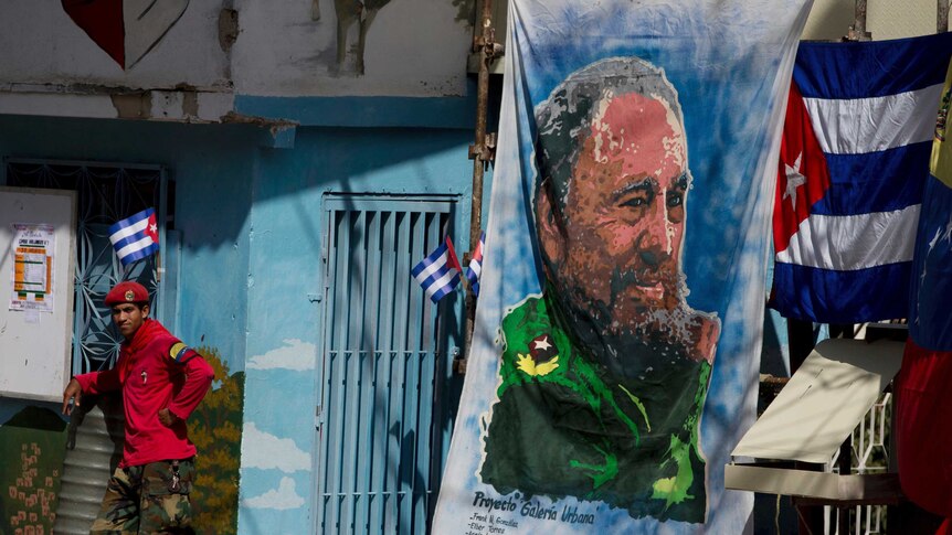 A militia member stands next to a painting of Fidel Castro.
