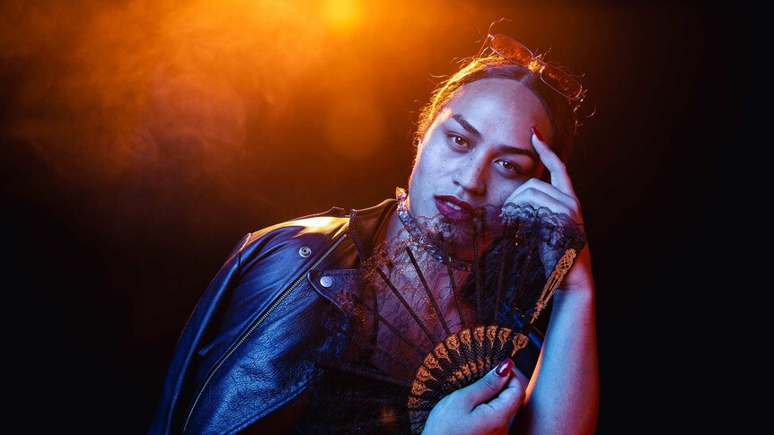A dramatic colour portrait of Kilia Tipa holding a fan and posing in front of dark background.