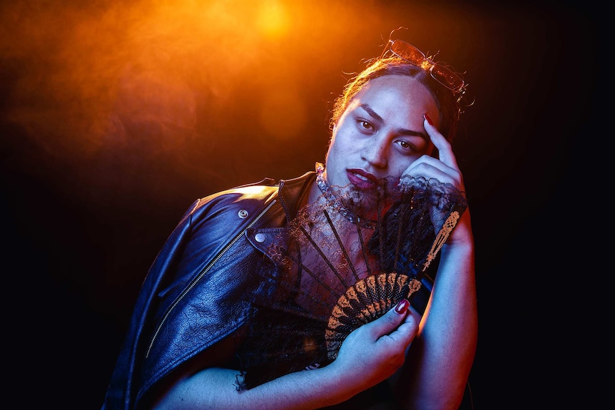 A dramatic colour portrait of Kilia Tipa holding a fan and posing in front of dark background.