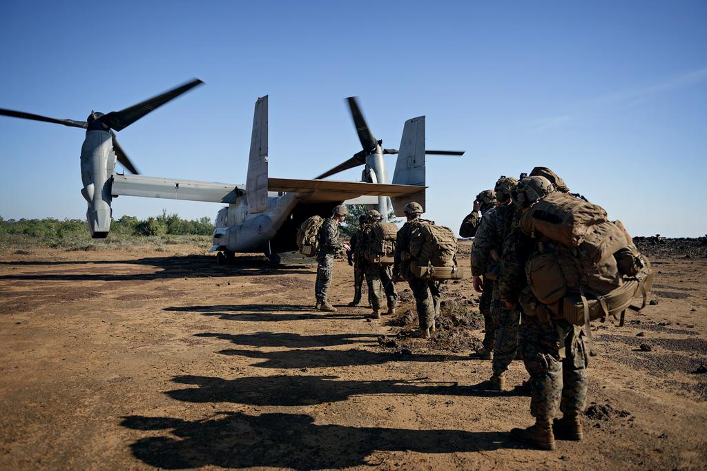 A line of marines walking ahead through dirt onto a waiting military aircraft