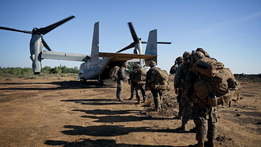 A line of marines walking ahead through dirt onto a waiting military aircraft
