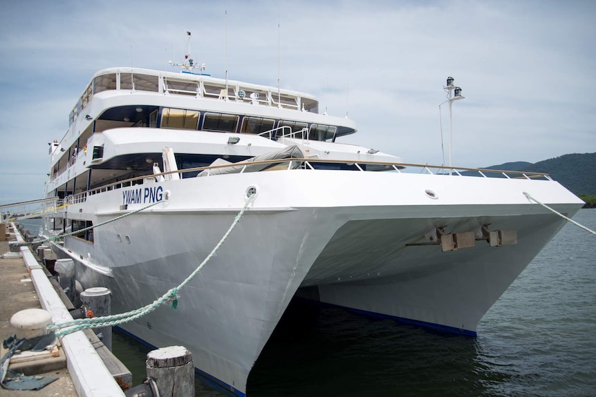 A large, white aluminium catamaran alongside a concrete wharf in Cairns.