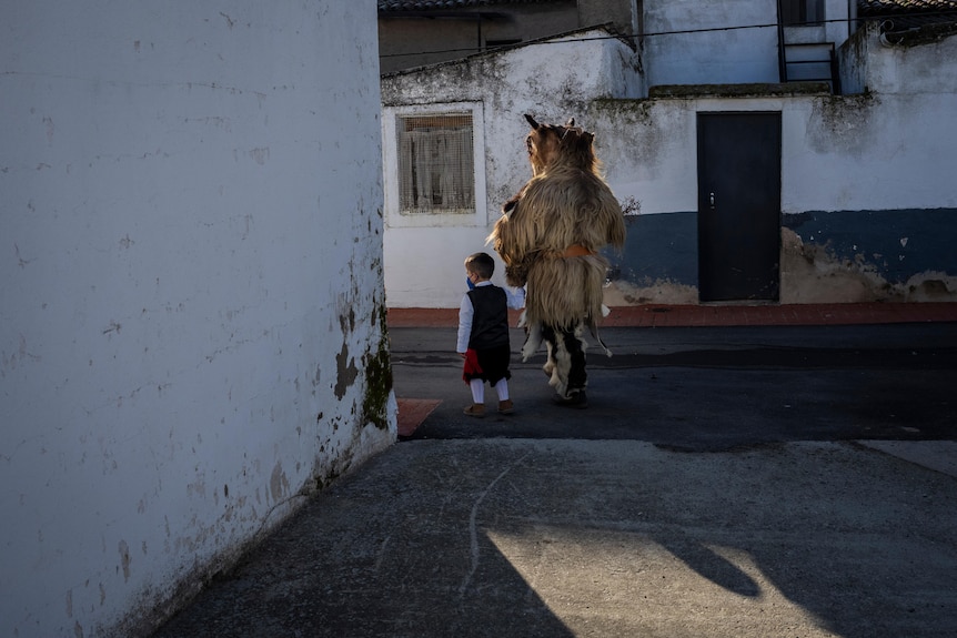 A small boy walks next to a man dressed as a wild animal.
