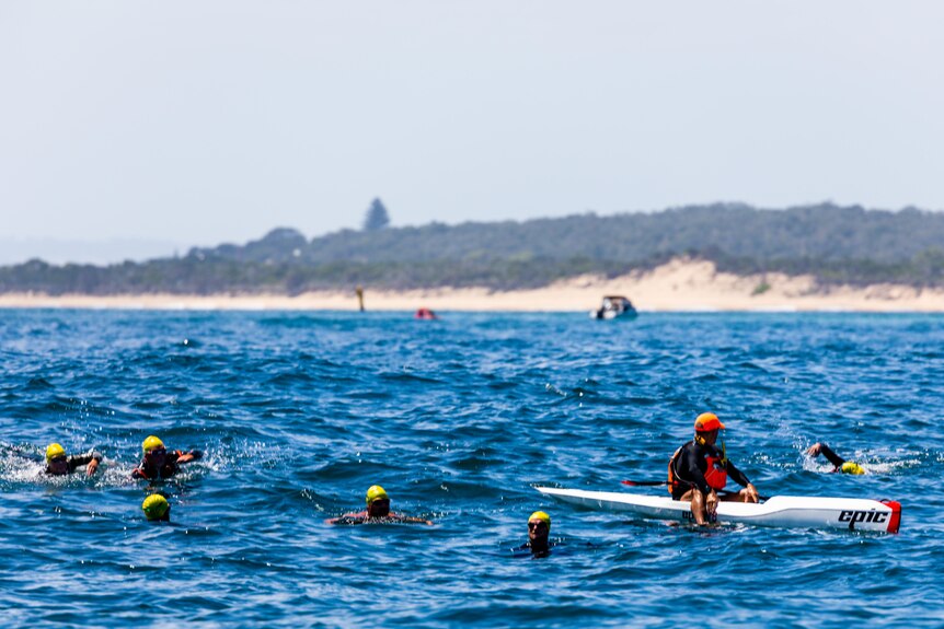 a group of swimmers in the water with a kayaker near them.