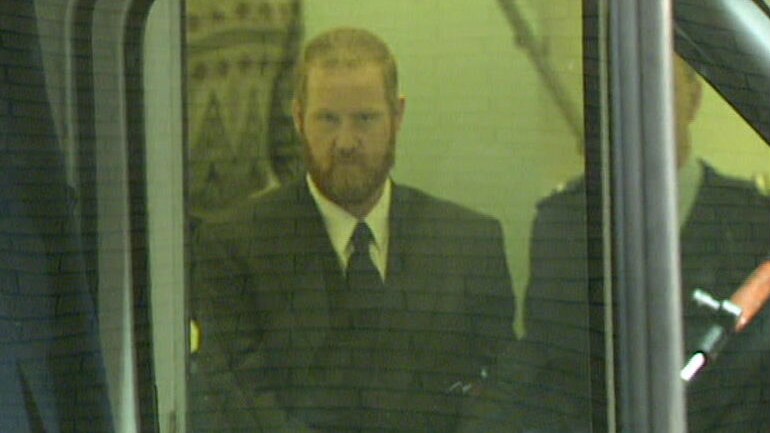 Craig Minogue seen through a window as he walks to the prison van.