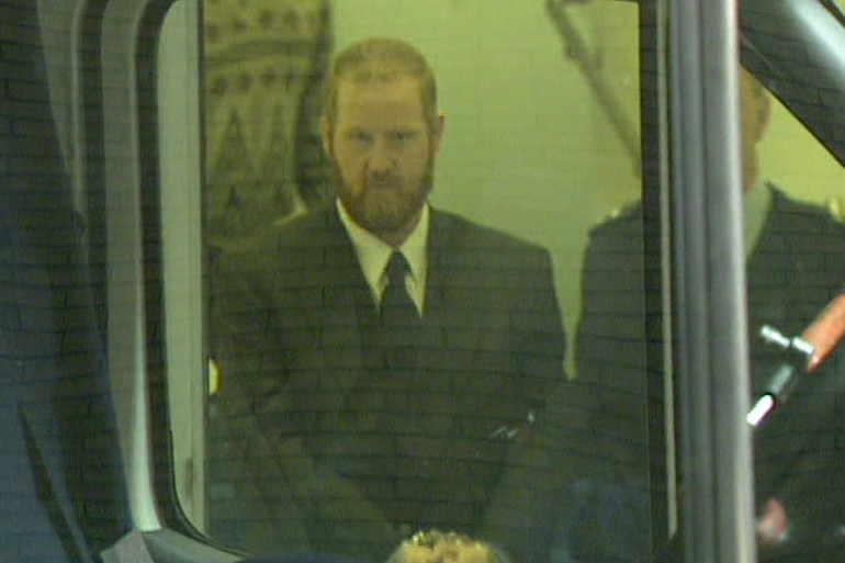 Craig Minogue seen through a window as he walks to the prison van.