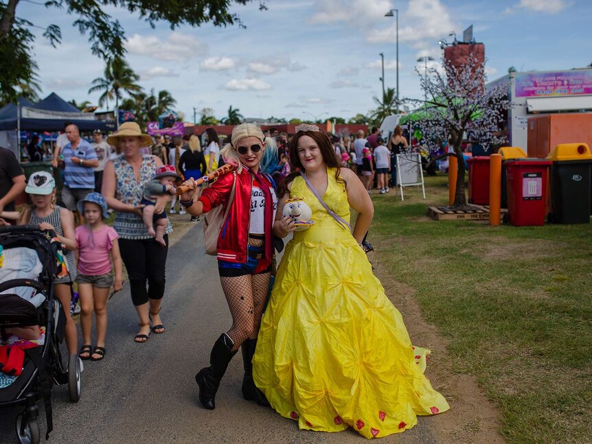 A woman stands with a baseball bat over her shoulder, dressed as Harley Quinn. Another stands next to her in a yellow ball gown.
