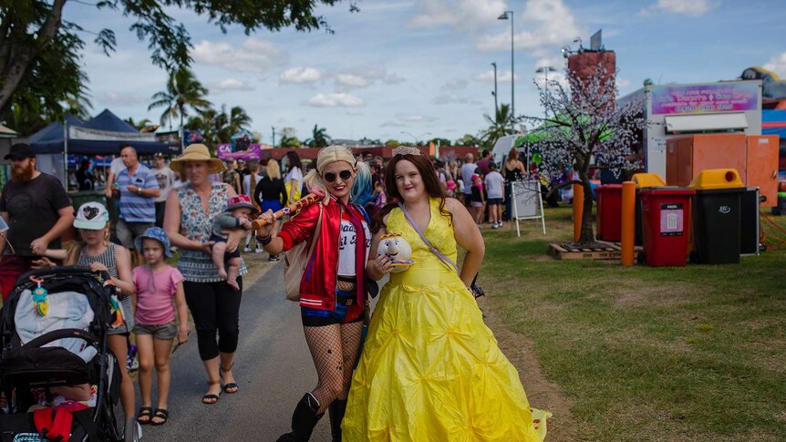 A woman stands with a baseball bat over her shoulder, dressed as Harley Quinn. Another stands next to her in a yellow ball gown.