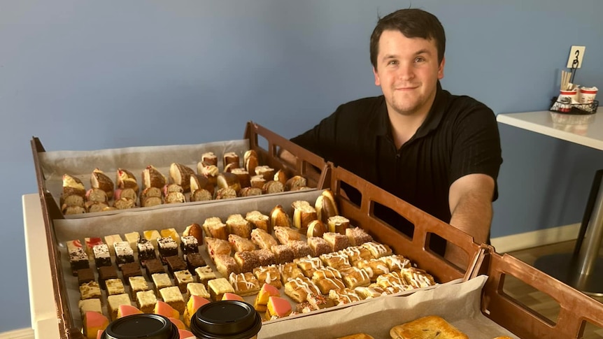 A man standing behind a tray of bakery items.