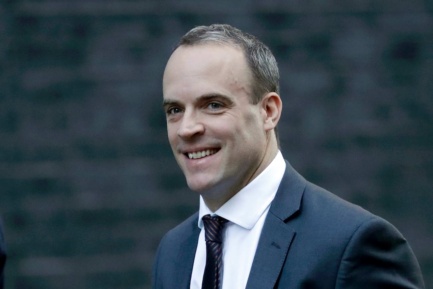 Dominic Raab, wearing a suit, smiles while walking