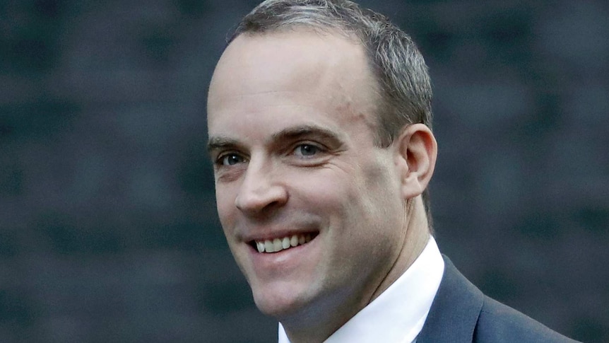 Dominic Raab, wearing a suit, smiles while walking