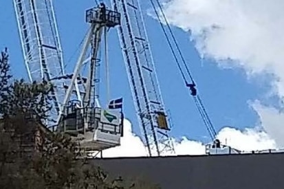 a eureka flag attached to a tower crane on a job site with a tree in the shot