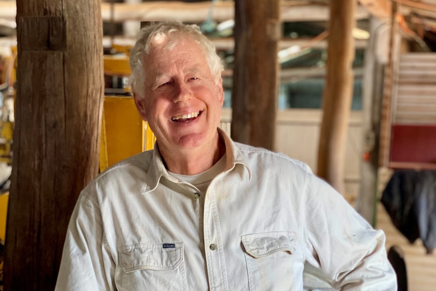 A man leans on a wool bale smiling at the camera