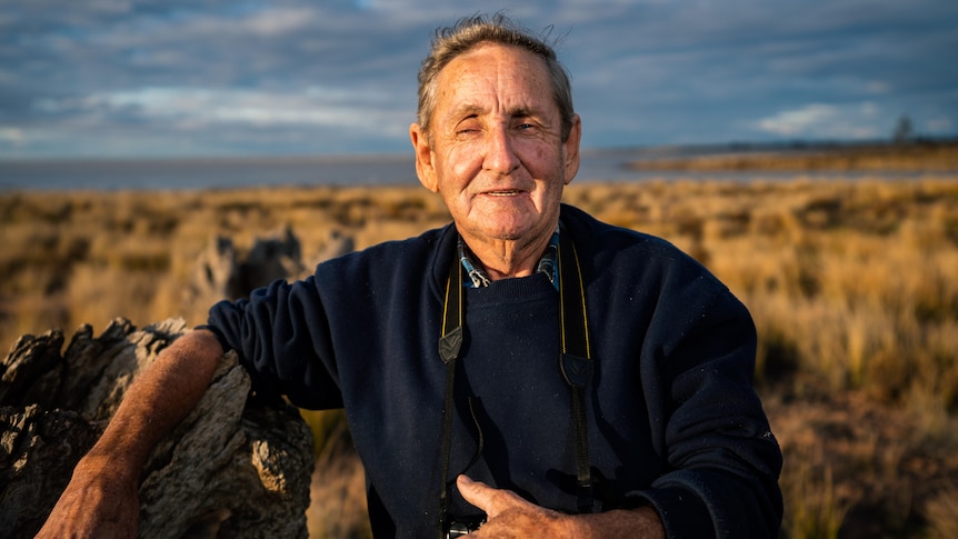 an older man in black shirt looking at camera with open landscape behins