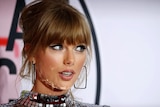 Taylor Swift looks to the right. She has smoky eye makeup, her hair is up and she is wearing a reflective mirror dress.