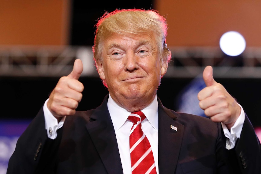 Donald Trump gives two thumbs up at podium.