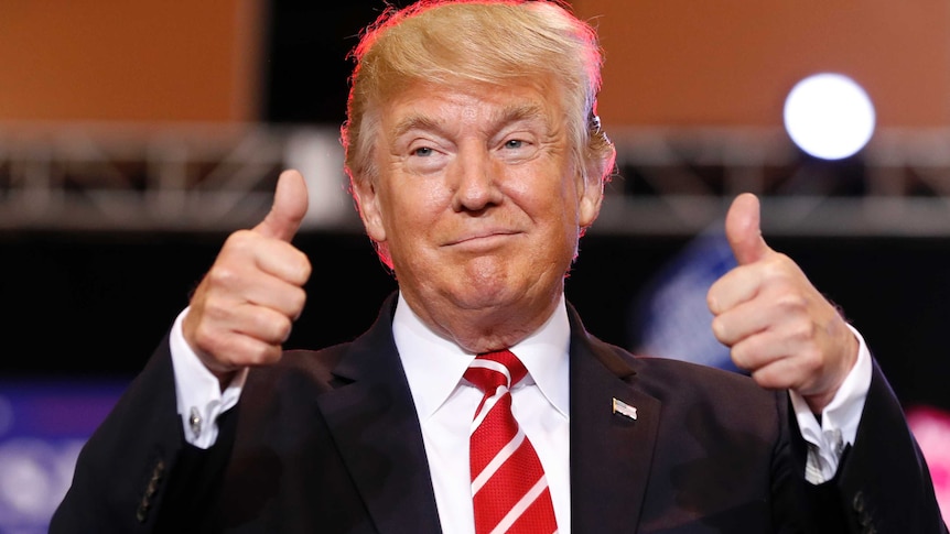 Donald Trump gives two thumbs up at podium.