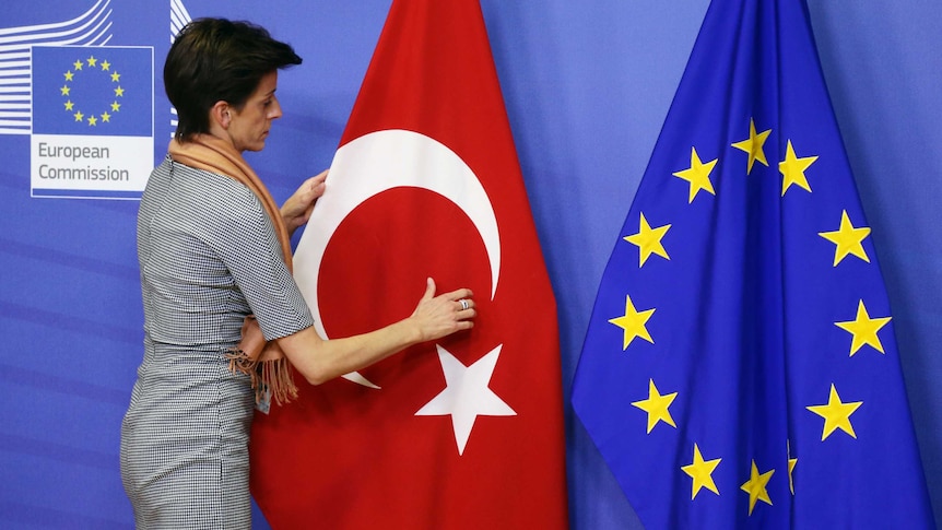 A woman adjusts the Turkish flag next to the European Union flag.