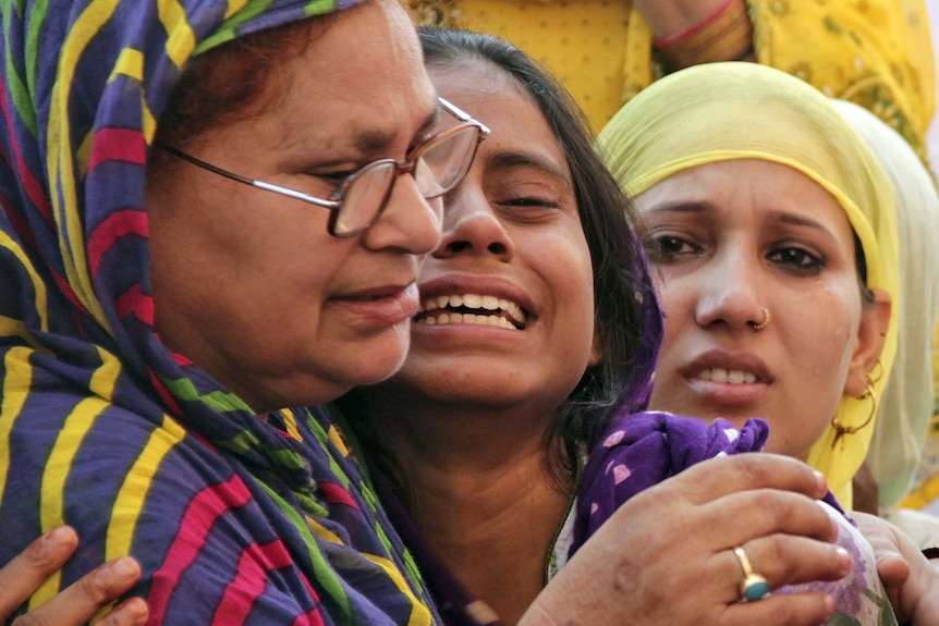 Three women cry while holding each other.