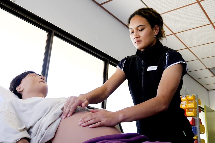 A student midwife over a pregnant dummy in a teaching hospital
