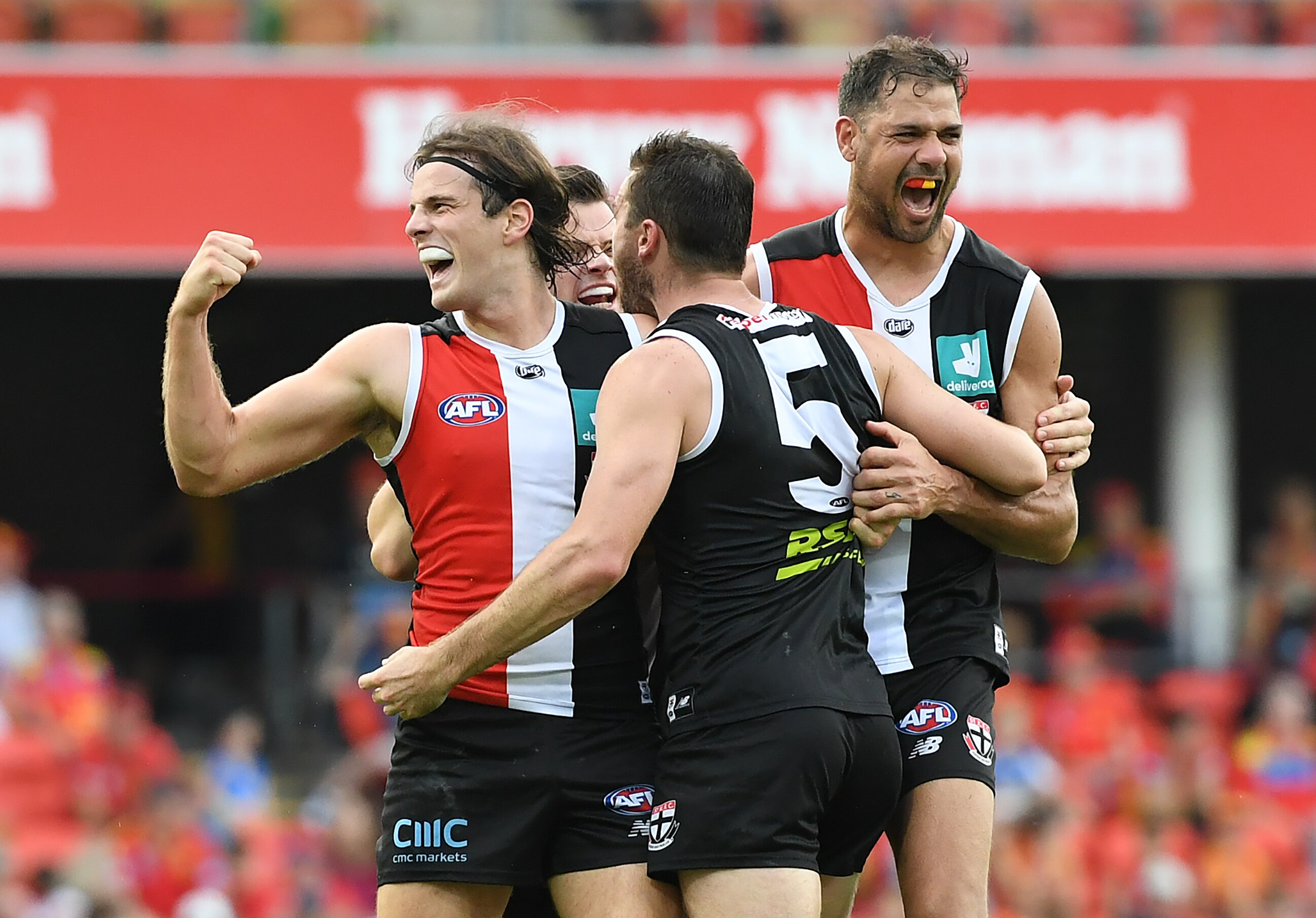 An AFL player pumps his fist in joy after scoring a goal as he is surrounded by teammates.