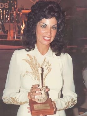a woman holding a golden guitar award, smiling at the camera in a white dress