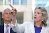 Clare O'Neil points into the distance at a press conference at parliament house. Andrew Giles is standing behind her