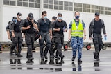 Men in fatigues and wearing masks walk along wet ground