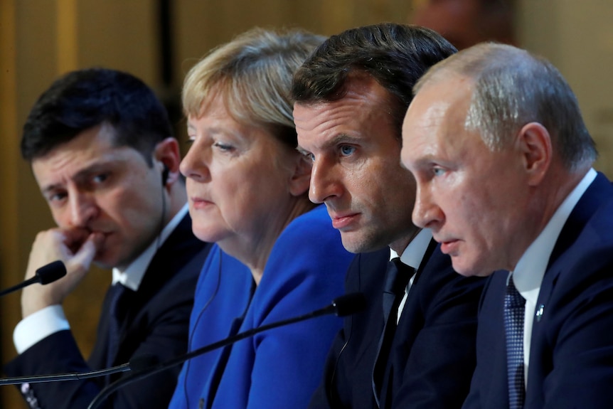 Volodymyr Zelenskyy, Angela Merkel, Emmanuel Macron and Vladimir Putin sit close together. Zelenskyy frowns looking toward Putin