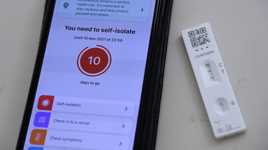 A phone screen displays a warning "You need to self-isolate". Next to it is a lateral flow or rapid antigen test with two lines