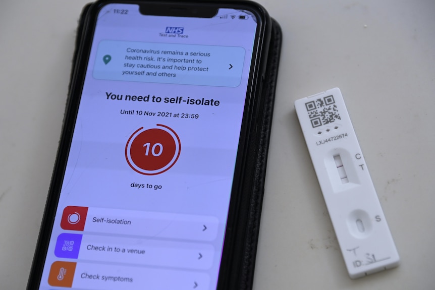 A phone screen displays a warning "You need to self-isolate". Next to it is a lateral flow or rapid antigen test with two lines