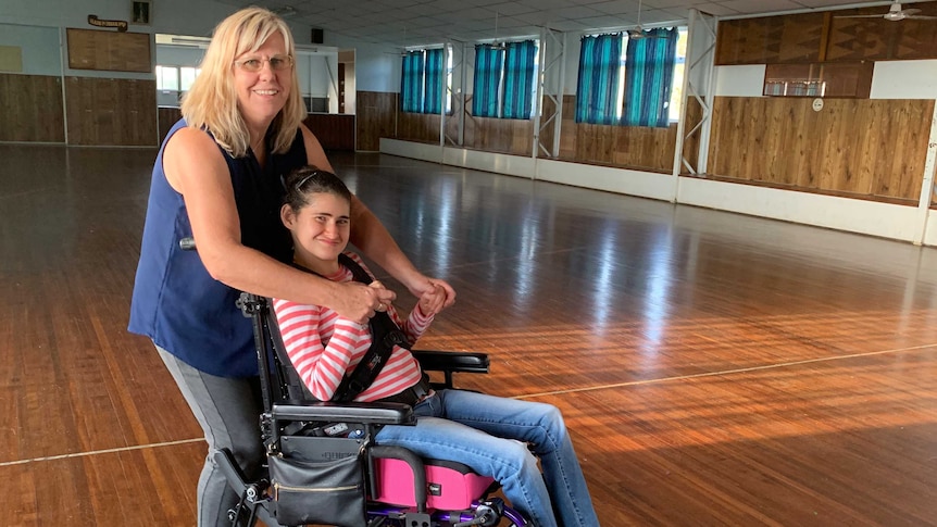 A young woman in a wheelchair dances with another woman.