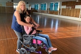 A young woman in a wheelchair dances with another woman.