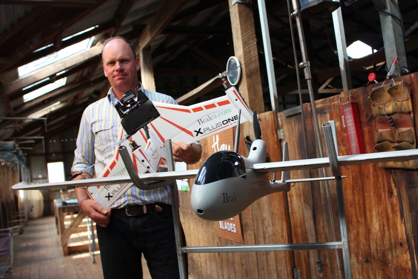 A man stands behind a drone on a stand.