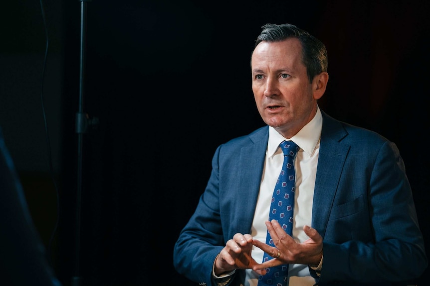 WA Premier Mark McGowan pictured seated in a studio with a dark background.