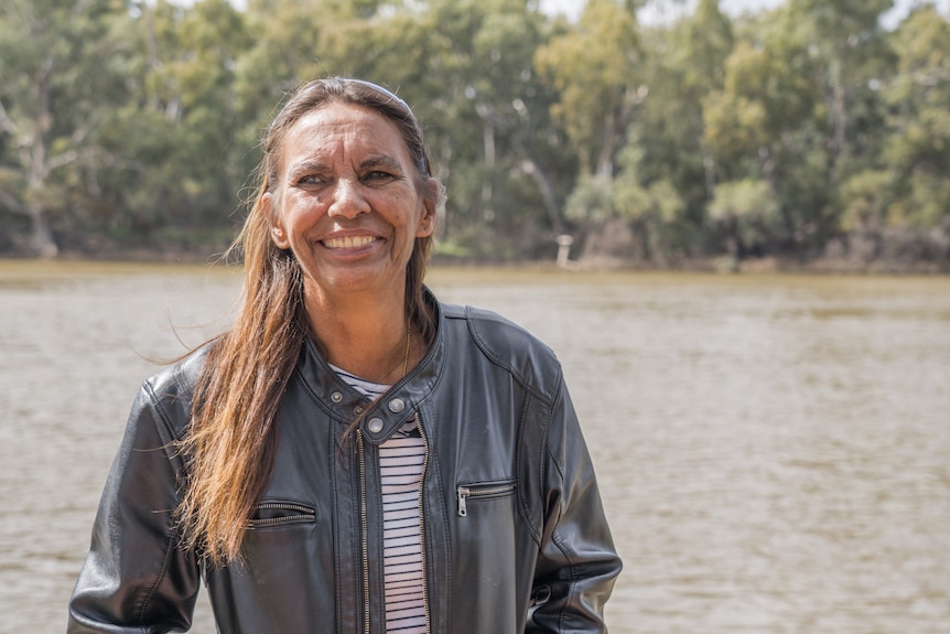 A woman smiles in front of a river.