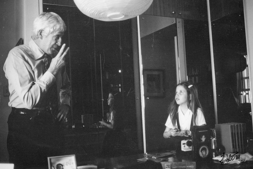 A black and white photo of young Ariana Neumann looks up at her father in the study of their Caracas home.